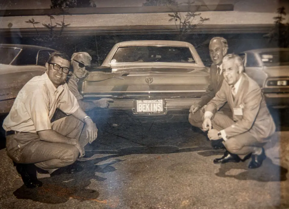 An old framed photo of three people beside a car with a Bekins plate