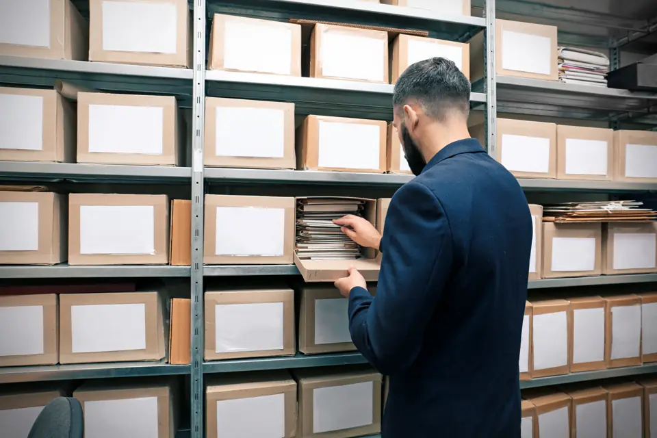 Rows of shelved archive file boxes with a man pulling documents