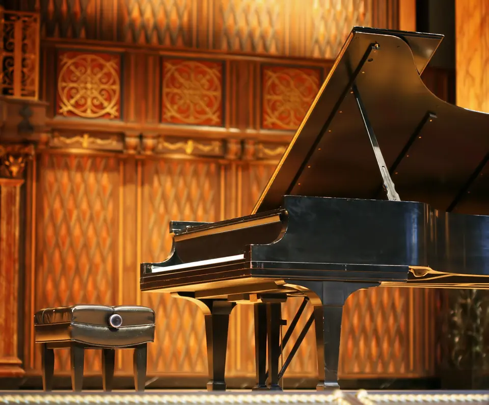 Black concert grand piano on a wood-panelled stage
