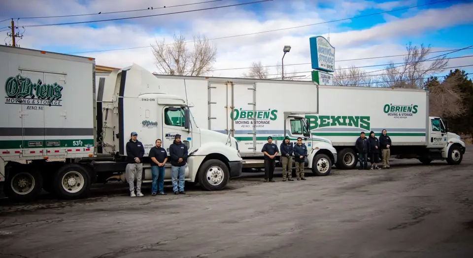 Three O'Brien's and Bekins trucks parked in a row in the yard with crew members beside them